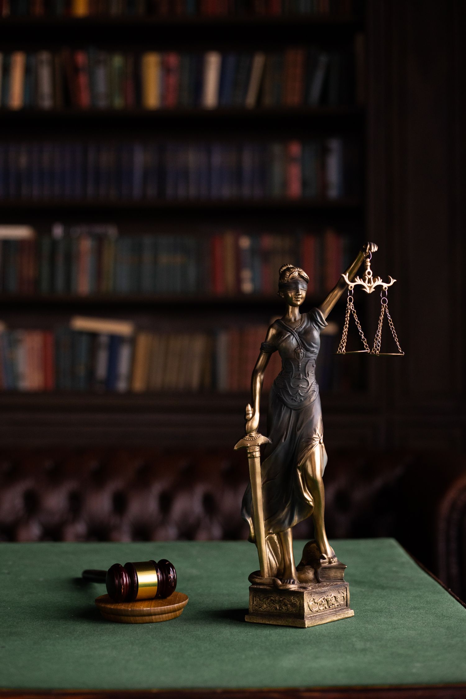 Bronze statue of Lady Justice holding scales and a sword, in a law library